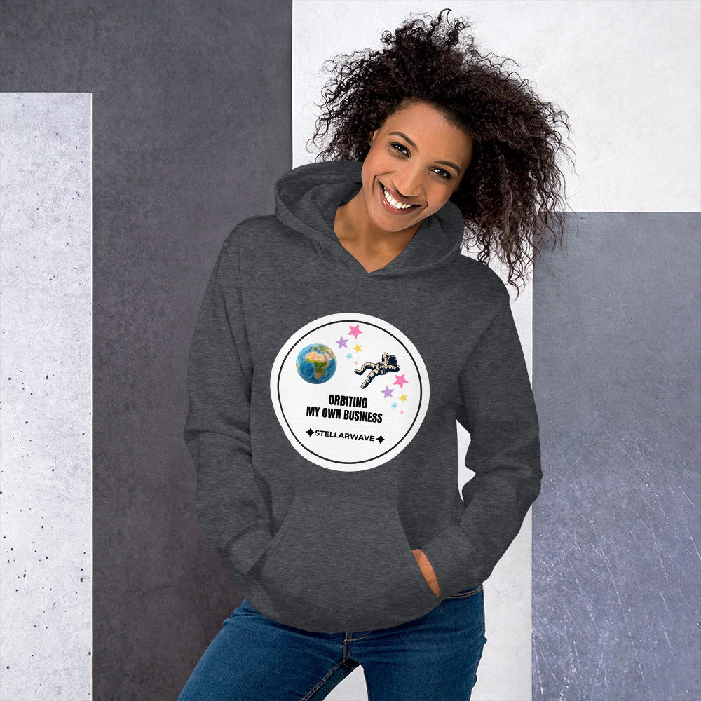 Woman smiling wearing a dark heather hoodie with a space-themed design featuring Earth, an astronaut, and stars with the text "Orbiting My Own Business" and "Stellarwave" in the Cosmos Comfort Collection - Orbiting My Own Business - Unisex Hoodie